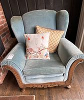 Front view of vintage teal velvet wingback armchair with two cushions and carved wooden detailing on arms and base.