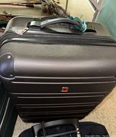 Photo of a large brown hard shell suitcase with a telescoping handle extended and a zippered compartment on the front.