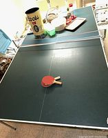 Wide shot of full ping-pong table with two paddles lying on the playing surface and a Coors can and other items on the table.