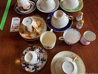 Photo showing all tea cups and saucers sets along with salt and pepper shakers and small demi-tasse cup on wooden table.