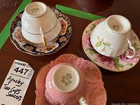 Photo shows three Aynsley tea cups and saucers with distinct floral patterns and gold trim, displayed upside down to show brand mark on bottom.