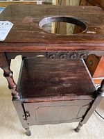 Front view of vintage wooden washstand side table showing circular cutout on top, turned legs, and cabinet door below.