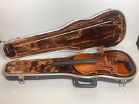 Violin inside open hard case lined with brown velvet, showing full violin and bow in case.