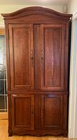 Front view of wooden cabinet with arched top and two sets of double doors against light-colored walls and floor