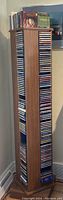 Full view of a wooden rotating CD tower packed with assorted CDs in jewel cases.