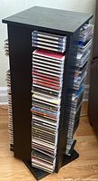 Full view of a black rotating CD rack loaded with about 50 assorted CDs in jewel cases, showing the lot's size and storage method.