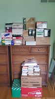 Wide shot showing a large quantity of envelopes boxes and bundles stacked on a wooden dresser and floor.