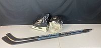 Full lot showing black CCM skates size 6.5 Y, black Cooper helmet with white cage in size M, and two Sherwood Bandit 51 hockey sticks.