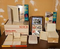 Displays entire assortment including boxed paper photo frames, Avery photo frame cards packages, Xerox paper box, and stacks of individual folded paper photo frames.