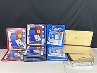 Photo showing multiple packages of ACCO Basic Report Covers in red, ACCO blue 2 pocket portfolios with fasteners, and light wood colored Oxford folders on a table.