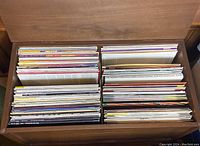 Wooden drawer divided into four sections holding numerous vinyl records upright, showing a variety of colors and spine text.