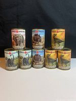 Eight sealed vintage dinosaur cans from the 'Prehistoric Series'. Labels show Triceratops, Stegosaurus, Tyrannosaurus, and Brachiosaurus dinosaurs.