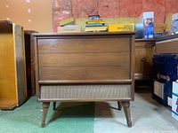 Front view of the vintage vinyl record storage cabinet showing the wood finish, tapered legs, and ribbed lower panel.