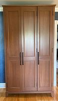 Front view of large wooden wardrobe with three paneled doors and vertical handles.