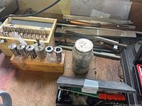 Photo showing multiple precision collets in wood holder, assorted bits in wooden box, and miscellaneous hardware on bench.