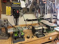 Workbench surface with drill press, milling vise, bench grinder, bench sander and arbor press arranged left to right