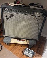 Front view of Fender Deluxe 112 Plus amp showing controls, silver grille, black tolex and cables on top.