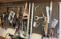 Wide view of pegboard in workshop with assortment of hand tools hung including saws, levels, rulers, clamps, wrenches, and screwdrivers.