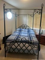 Full view of the black metal four poster full bed frame set up with mattress in a bedroom. Shows headboard, footboard, and posts.