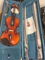 Violin inside the open blue plush-lined case with two bows and instruction sheet.