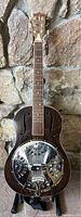 Front view of resonator guitar showing dark wood top, metal resonator cover and maple neck