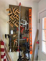 Pegboard showing various clamps with wooden handles, quick-grip clamps, and orange spirit level hanging vertically.