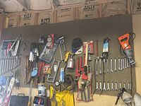 Wide view of assorted hand tools including wrenches, pipe wrenches, spray gun, and reciprocating saw hung on pegboard