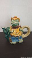 Front view of ceramic alligator teapot with cowboy outfit and cactus spout.