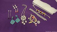 Full view of all jewelry pieces arranged on purple cloth, showing necklaces, bracelets, and earrings.