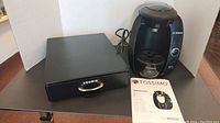 Bosch Tassimo coffee maker with Keurig pod holder side by side on table.