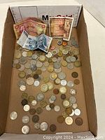 Box with many assorted foreign coins and paper money visible.