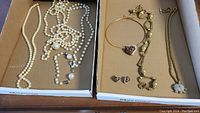 Two trays with multiple necklaces and faux pearls, including gold-colored and pearl bead necklaces, displayed in cardboard trays.