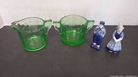 Front view of green Depression glass cream pitcher and sugar bowl along with blue and white Delft salt and pepper shakers shaped as man and woman figurines.