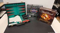 Backgammon set open showing playing surface with red and black points and accessories. Boxed Cranium and Lord of the Rings Trivial Pursuit board games alongside.