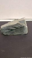 Rough and smooth jadeite rock placed on a flat black surface, showing the texture and color of the stone.