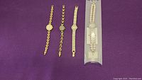 Four ladies wristwatches laid out on purple fabric; gold-tone metal bands and one packaged pearl bracelet watch visible.