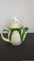 Side view of the teapot showing the rabbit figure on the lid and leaf detailing.