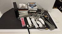 Photo of Nintendo Wii console, controllers, sensor bar, cables, and game discs showing included items in lot.