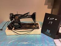 Side view of antique Singer sewing machine mounted on a white wooden base with attached power cord and foot pedal, placed on a blue surface.