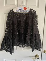Front view of black lace short top with bell sleeves hanging on hanger
