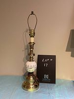 Full view of the brass and ceramic table lamp against a neutral wall with a tag indicating lot number 17.
