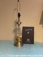 Full view of brass and glass table lamp without shade showing base, glass body, and harp.