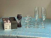 Photo showing six champagne flutes, four champagne coupes, and the boxed Kuraidori red wine decanter on a blue surface.