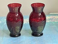 Photo showing both cherry red glass vases side by side on a textured light blue surface with reflective background.