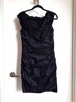 Front side of black cocktail dress showing ruching and sleeveless design on hanger.