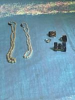 Two strands of faux pearl necklaces and six costume rings on a blue textured background.