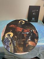 Round modified limited edition 'Crucifixion' print by Harmonia Rosales on fabric surface with lighting reflecting details of artwork and halos.