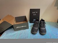 Pair of women's Eddie Bauer Hunt Pac Mid boots shown with original box. Boots are black with quilted fabric uppers and rubber waterproof shell with laces.