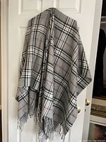 Front view of grey and charcoal tartan poncho showing plaid pattern and fringe at hem.