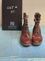 Front view of the pair of Fly London leather lace-up boots in distressed red/brown color with box.